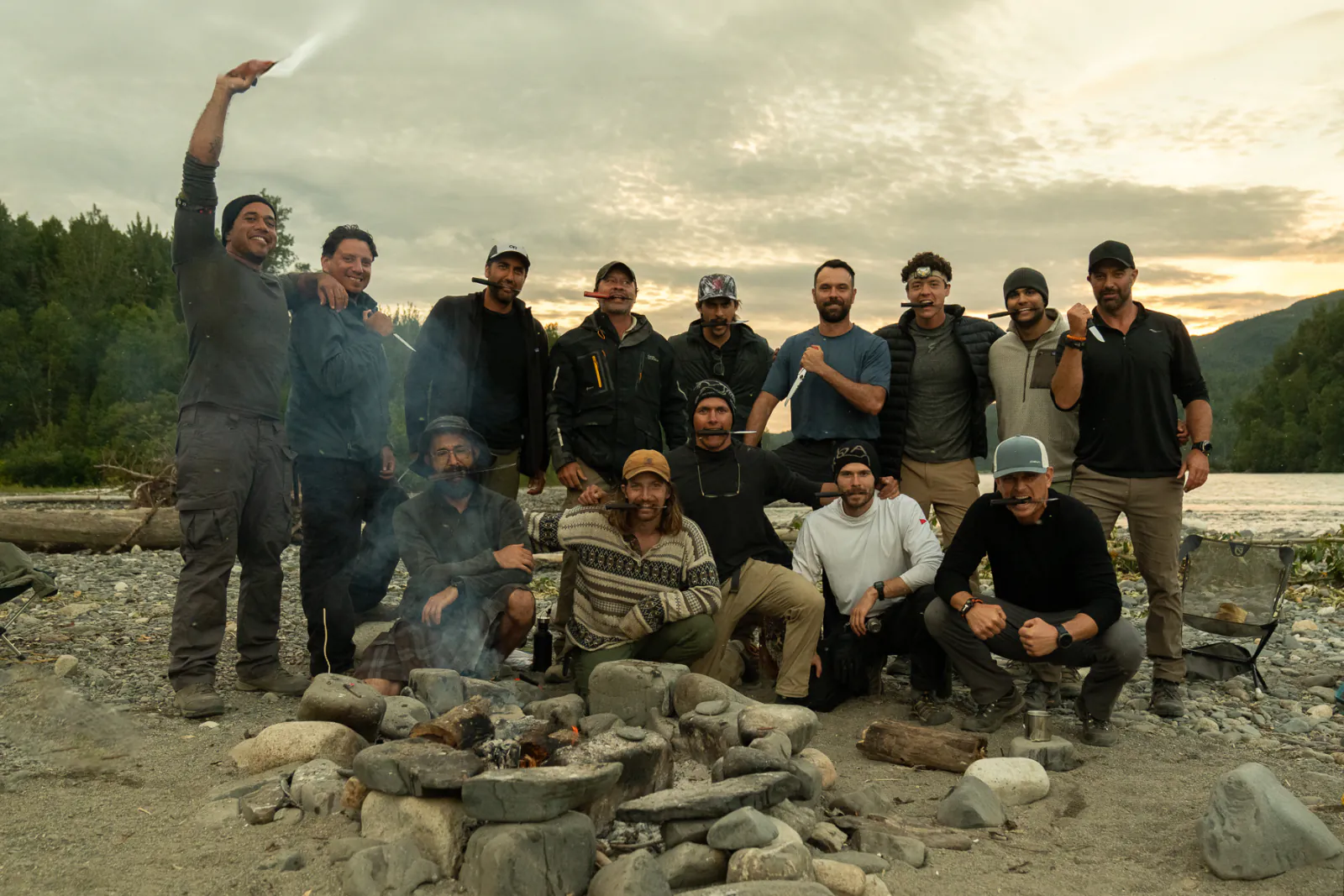The full group from the Alaska retreat gathered around a campfire on a river bar at sunset