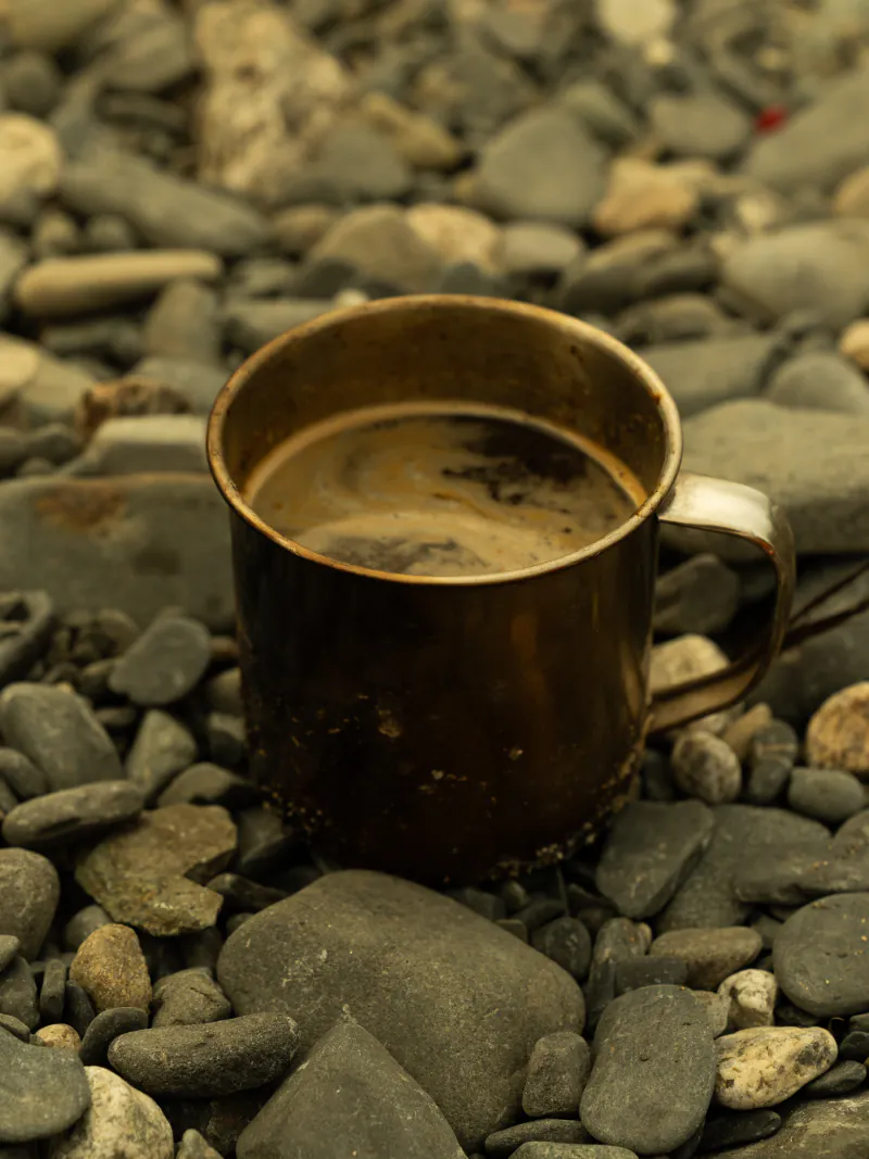 Camp coffee in a battered enamel mug resting on river stones